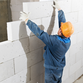Muratore con casco arancione che costruisce un muro di blocchi bianchi in un cantiere edile